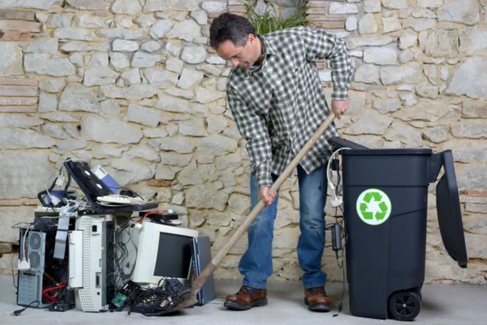A man organizes a room, disposing of items in a recycling bin, part of an e-waste removal service in Seattle, WA.